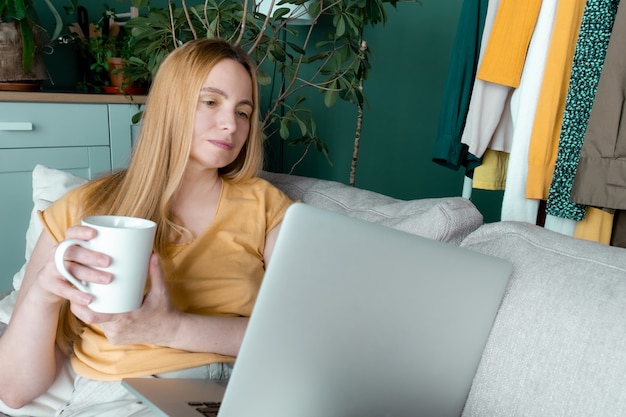 40 50 plus Frau mittleren Alters blonde Kleidung gelb grün Laptop online Sofa Zimmer
