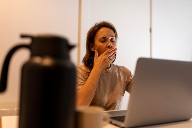 40-jährige Frau gähnt müde zu Hause oder im Büro mit Laptoparbeit spät im Büro