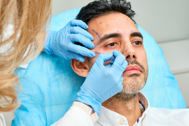 45-jähriger dunkelhaariger Mann in einer Schönheitsklinik mit mit Strichen bemaltem Gesicht zur Behandlung
