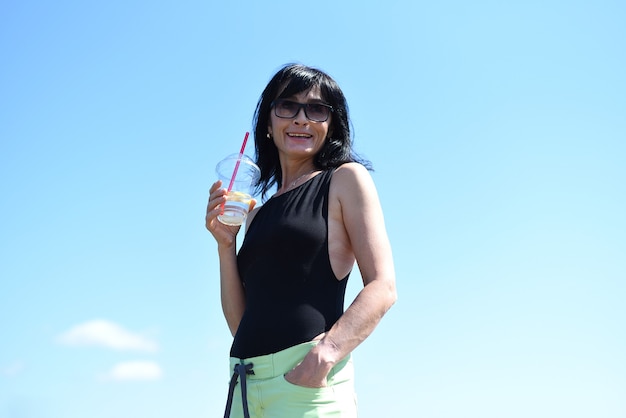 45 Jahre alte Russin, die Limonade trinkt und gegen den blauen Himmel steht