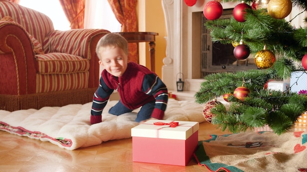 4K-Aufnahmen eines glücklich lächelnden kleinen Jungen öffnen sein Weihnachtsgeschenk vom Weihnachtsmann und nehmen eine Spielzeugeisenbahn heraus. Kinder, die an Winterferien und an Feiertagen Geschenke und Geschenke erhalten