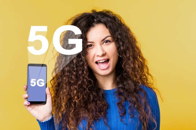 5G-Netzwerk Drahtlose Kommunikation Mobiles Internet IKT digitale Zukunft Innovative Technologie Aufgeregte Frau zeigt Smartphone mit weißem Symbolhologramm isoliert auf Orange