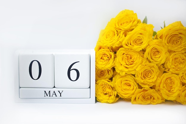 6 de mayo en un calendario de madera blanca y un ramo amarillo de rosas yacen uno al lado del otro