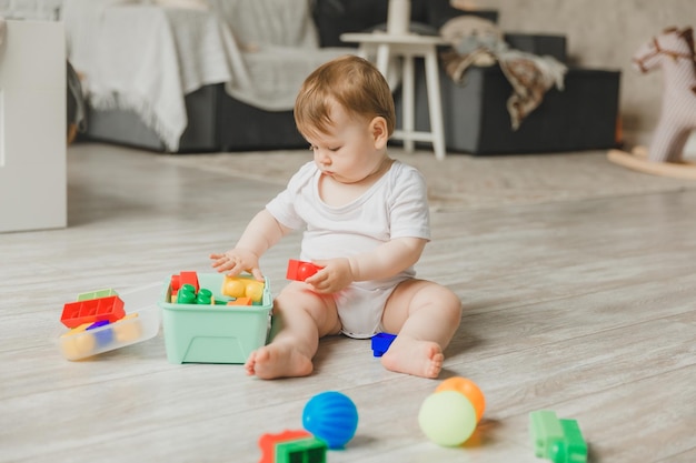 69 Monate altes Baby spielt mit einer bunten Regenbogen-Spielzeugpyramide und sitzt in einem weißen, sonnigen Schlafzimmer. Spielzeug für Kleinkinder. Inneneinrichtung für Kinder. Ein Kind mit einem Lernspielzeug