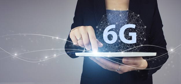 6G-Netzwerk Internet Mobile Wireless-Geschäft. Weiße Tablette in der Hand der Geschäftsfrau mit digitalem Hologramm 6G-Zeichen auf Grau. Das Konzept des 6G-Netzes, des mobilen Hochgeschwindigkeitsinternets, der Netze der neuen Generation.