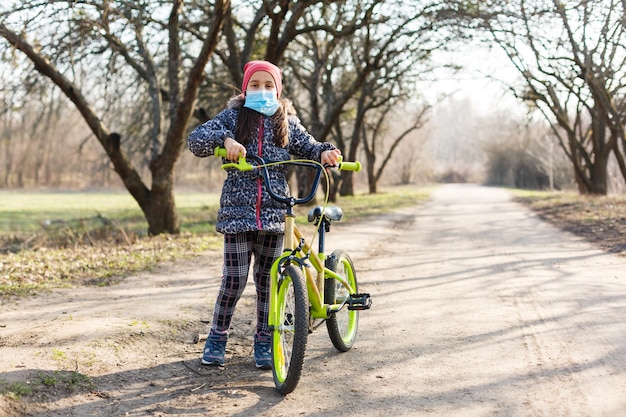 7 años de edad, niña feliz, paseo en bicicleta en el parque en casa y con máscara de protección para proteger los síntomas del virus de la pandemia pm2.5 y Coronavirus Covid-19 Ejercicio deportivo para la salud.