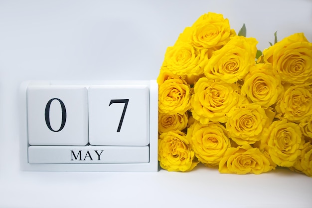 7 de mayo en un calendario de madera blanca y un ramo amarillo de rosas yacen uno al lado del otro