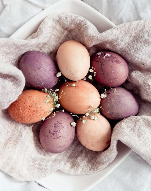 8 coloridos huevos de gallina festivos de Pascua yacen en círculo sobre una toalla de textura gris decorada con pequeñas flores en un plato blanco vista desde arriba