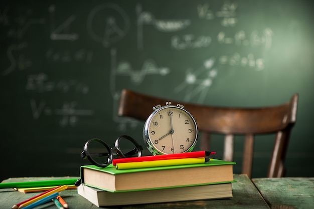 8 Uhr Zurück zum Schulkonzept. Wecker auf Büchern mit Tafel im Hintergrund