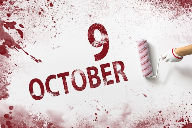 9 de outubro. Dia 9 do mês, data do calendário. A mão segura um rolo com tinta vermelha e escreve uma data do calendário em um fundo branco. Mês de outono, conceito de dia do ano.