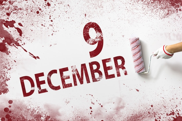 9 de diciembre. Día 9 del mes, fecha del calendario. La mano sostiene un rodillo con pintura roja y escribe una fecha del calendario sobre un fondo blanco. Mes de invierno, concepto de día del año.