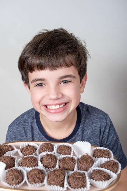 9-jähriges Kind mit einem Tablett mit mehreren brasilianischen Fudgebällchen und einem breiten Lächeln