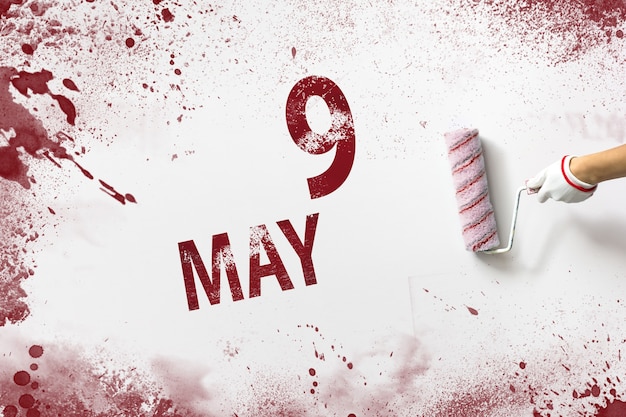 9. Mai. Tag 9 des Monats, Kalenderdatum. Die Hand hält eine Rolle mit roter Farbe und schreibt ein Kalenderdatum auf einen weißen Hintergrund. Frühlingsmonat, Tag des Jahreskonzepts.