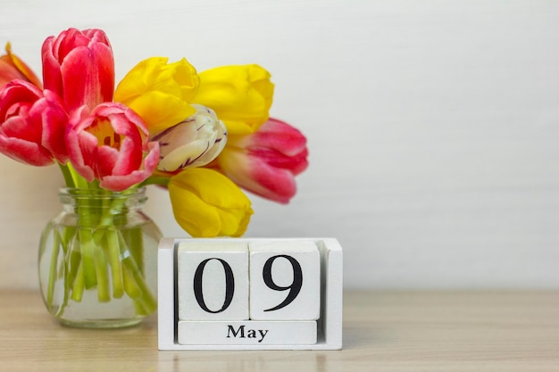 9 de mayo en un calendario de madera junto a un ramo de tulipanes. Un día del mes de primavera.