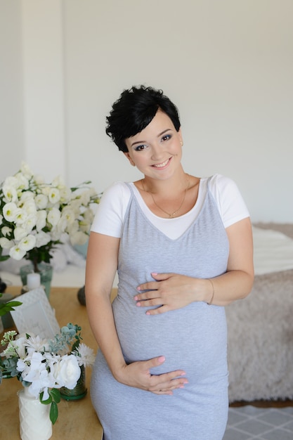 9 meses, niña embarazada con flores en casa. Esperando bebé. Vientre de mujer embarazada. Feliz futura madre.