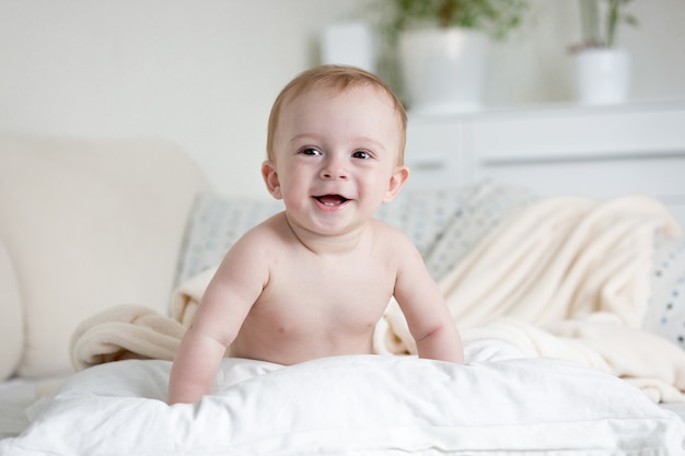 9 Monate altes glückliches Baby krabbelt über Kissen auf dem Bett