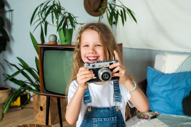 A adolescente branca tira fotos em uma câmera retrô e ri hobby para crianças e infância feliz