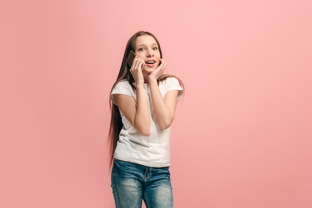 Foto a adolescente feliz em pé e sorrindo contra a parede rosa