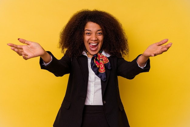 A aeromoça jovem afro-americana isolada em um fundo amarelo se sente confiante em dar um abraço para a câmera.