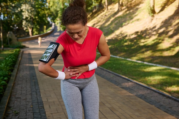 A afro-americana esportista de corrida segura seu estômago tem cãibras laterais durante o treinamento de corrida Conceito de lesões esportivas