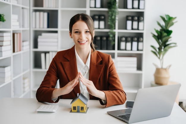 A agente imobiliária está a usar as mãos para proteger o telhado vermelho para o conceito de investimento imobiliário sobre a compra de casas no escritório no escritório xA