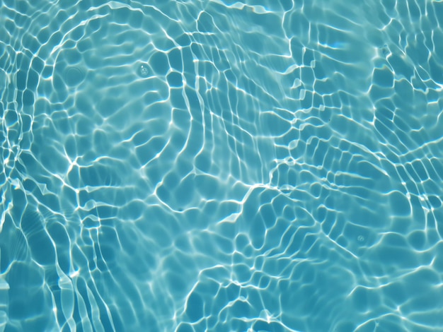 A água azul de uma piscina com ondulações e o sol refletindo na superfície.