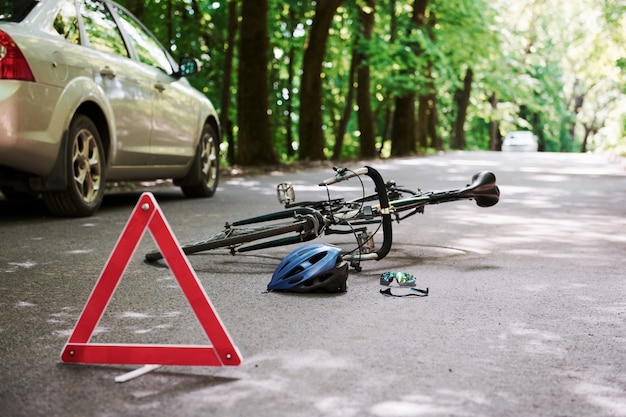 A ajuda está a caminho. Bicicleta e acidente de carro prateado na estrada na floresta durante o dia