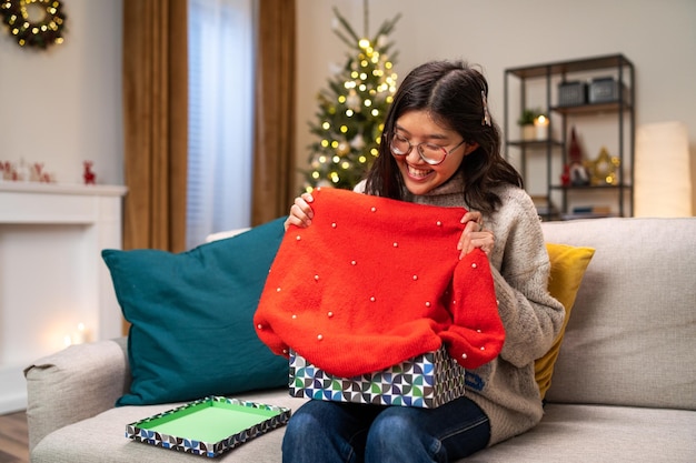A alegria de receber um presente de natal, uma mulher alegre desembrulha um suéter vermelho de inverno de uma caixa