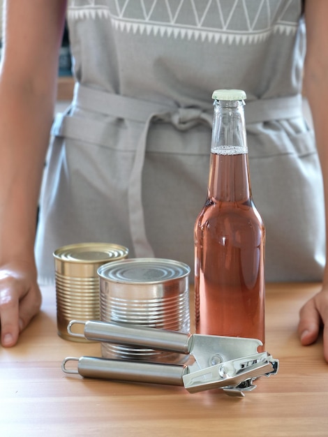 A anfitriã em um avental de cozinha cinza demonstra uma garrafa e um abridor de latas