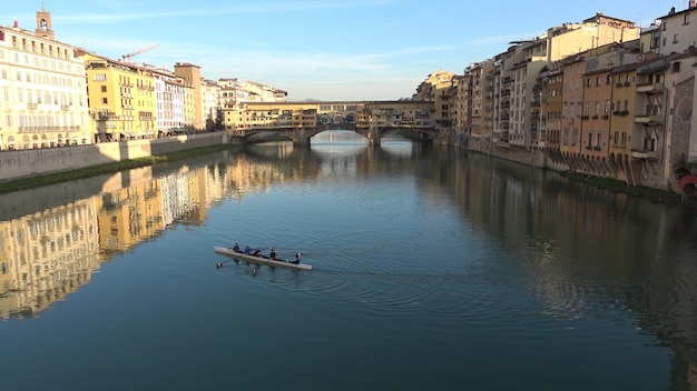 A antiga ponte de arco segmentar da ponte vecchio com lojas e habitações sobre o rio arno, em florença, itália, reflexos dourados na água