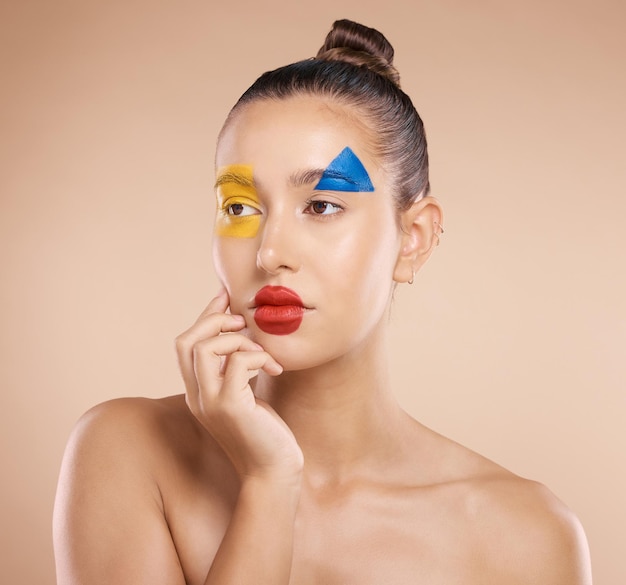 A arte da beleza e o retrato da mulher pintam no rosto maquiagem criativa e auto-expressão séria Criatividade em cuidados com a pele e mão tocando a bochecha com cosméticos de forma de cor artística na jovem linda