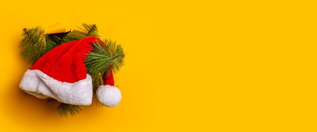 A árvore de Natal com um chapéu de Papai Noel aparece por um buraco em um fundo amarelo. Conceito de ano novo e véspera de Natal. Bandeira.