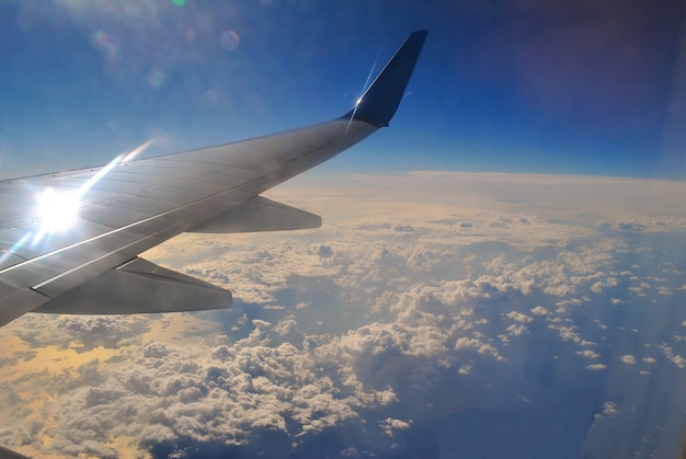 A asa de um avião voando alto acima das nuvens e acima do mar contra um céu azul brilhante.