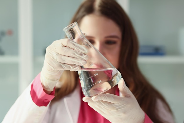 A assistente de laboratório olha para o frasco de água e verifica a água