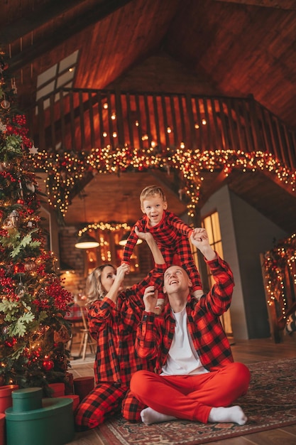 A autêntica família feliz e fofa em pijama xadrez vermelho passa tempo juntos no lodge Xmas decorado