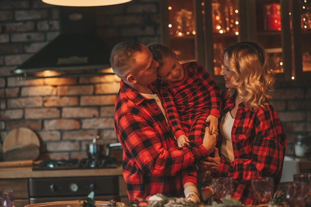 A autêntica família feliz e fofa em pijama xadrez vermelho passa tempo juntos no lodge Xmas decorado