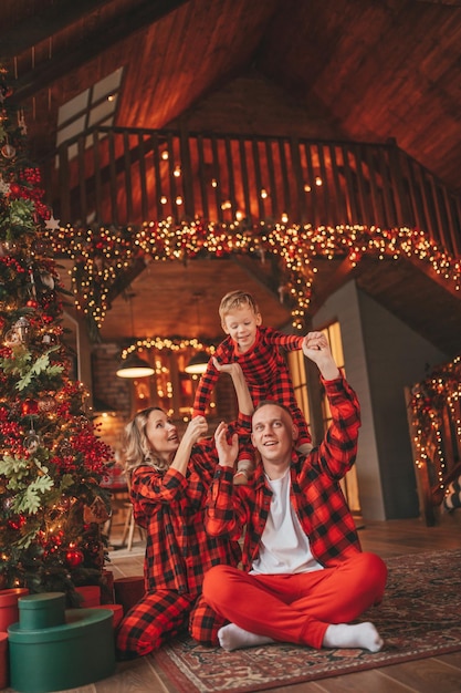 A autêntica família feliz e fofa em pijama xadrez vermelho passa tempo juntos no lodge xmas decorado