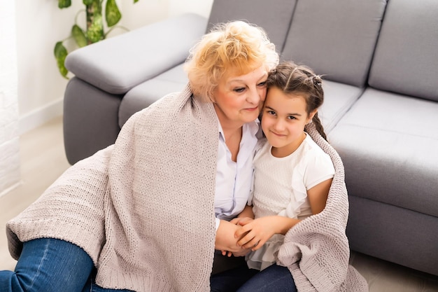 A avó sênior feliz senta-se no sofá na sala de estar abraçando a neta pré-escolar bonitinha, sorrindo a avó madura abraça o pequeno neto, mostra amor e cuidado, conceito de união.