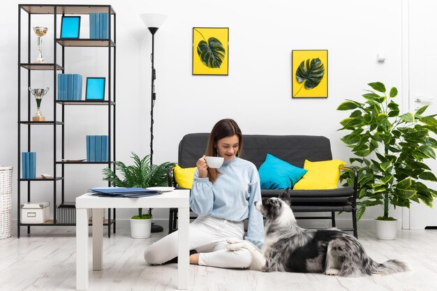 Foto a babá está sentada no chão bebendo café e o cachorro está deitado ao lado dela olhando para o seu border collie inteligente sheepdog design interior moderno do apartamento