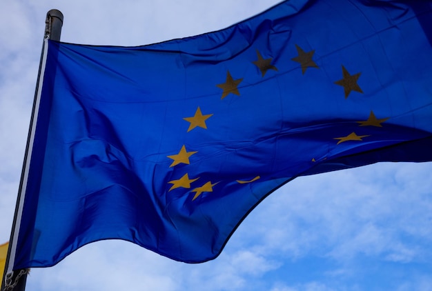 A bandeira da União Europeia acena no mastro com céu azul e nuvens para o plano de fundo Fechado com detalhes