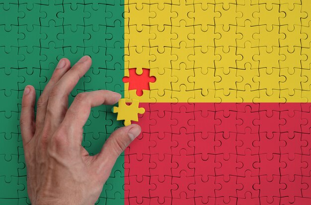 A bandeira do Benin é retratada em um quebra-cabeça, que a mão do homem completa para dobrar