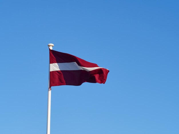 A bandeira nacional da Letônia agitando no vento na moldura horizontal do mastro da bandeira