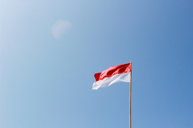 A bandeira vermelha e branca bendera indonésia está vibrando ao vento no céu azul