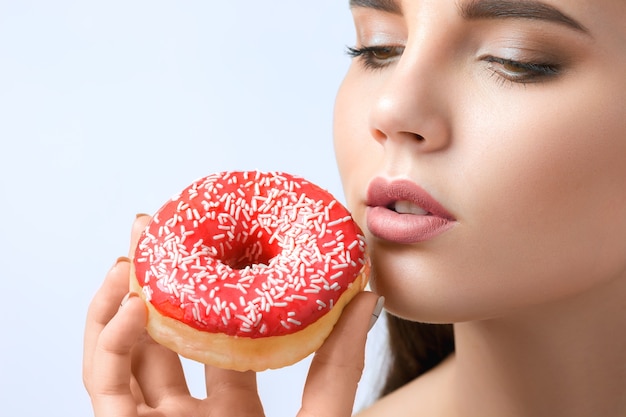 A bela mulher mordendo um donut no fundo cinza do estúdio