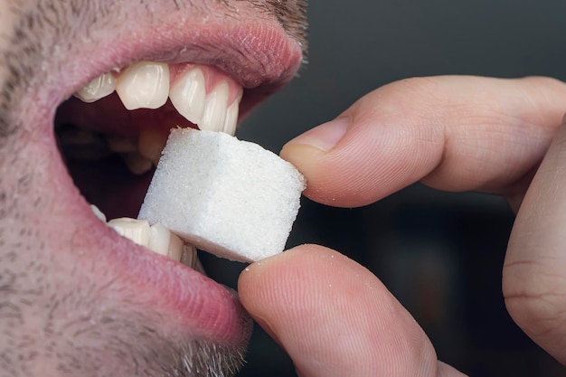 A boca do homem com dentes brancos morde um cubo de açúcar branco closeup