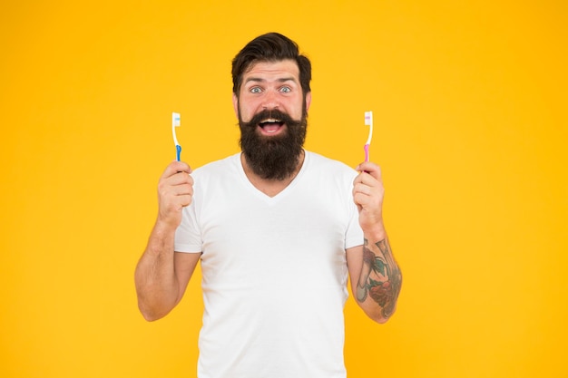 A boca importa Homem barbudo sorriso feliz com escovas de dentes Hipster feliz segura escovas fundo amarelo Higiene dental Clínica odontológica Cuidados dentários suaves Saúde bucal