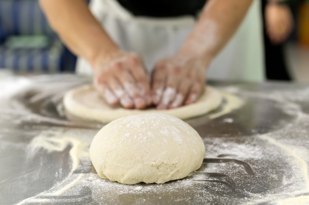 A bola da massa da pizza na tabela com mãos do cozinheiro chefe amassa a massa no fundo.