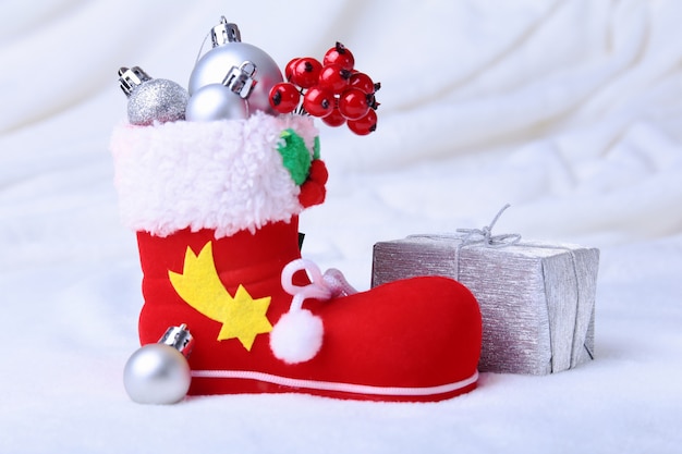 Foto a bota do papai noel vermelho com presentes de natal em fundo de neve. composição de boas festas.