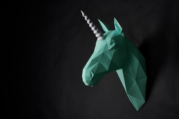 A cabeça do unicórnio verde de origami que pendura na parede preta.