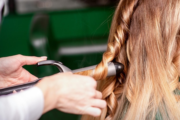 A cabeleireira está enrolando o cabelo para uma jovem caucasiana de cabelos castanhos em um salão de beleza